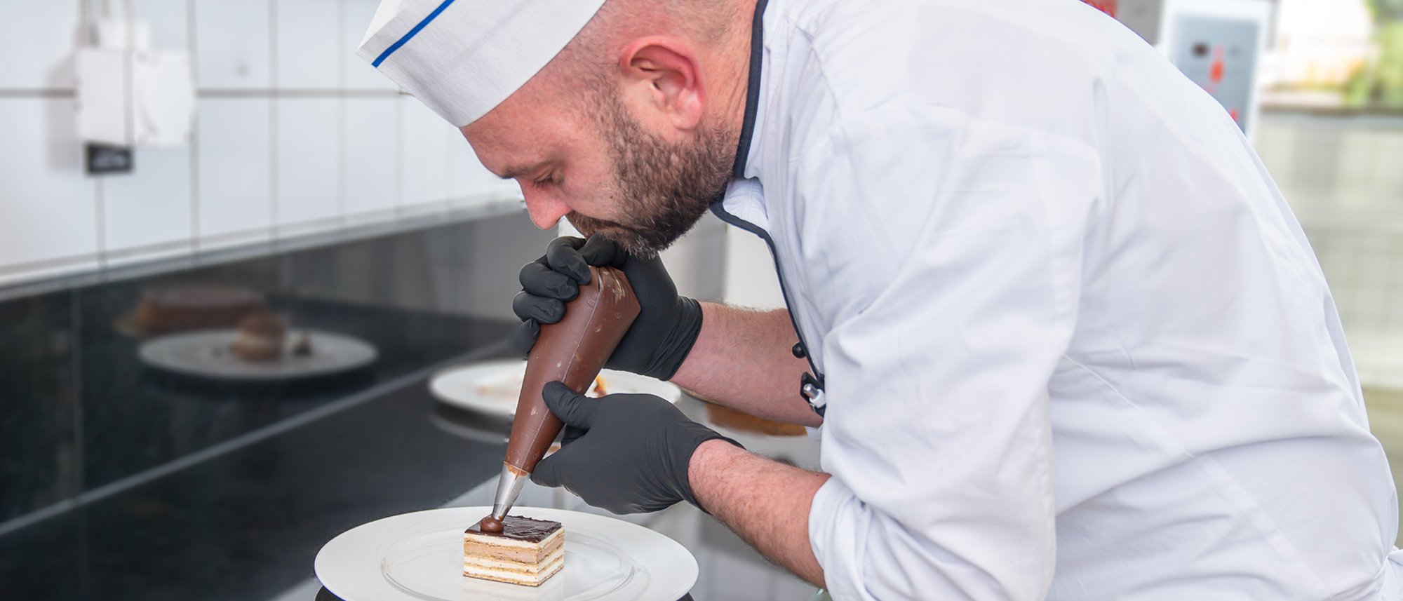 Küchenmitarbeitender verziert ein Dessert mit Schokolade in einer Küche.