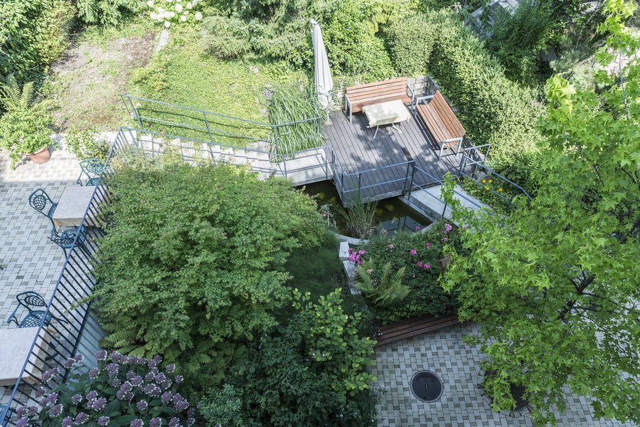 Es ist der Innenhof der Casavita Hasenbrunnen sichtbar mit Sitzbereichen aus Metallstühlen und Holztischen sowie dichte Büsche, Blumen und Bäume welche die verschiedenen Eben des Innenhofes umgeben.
