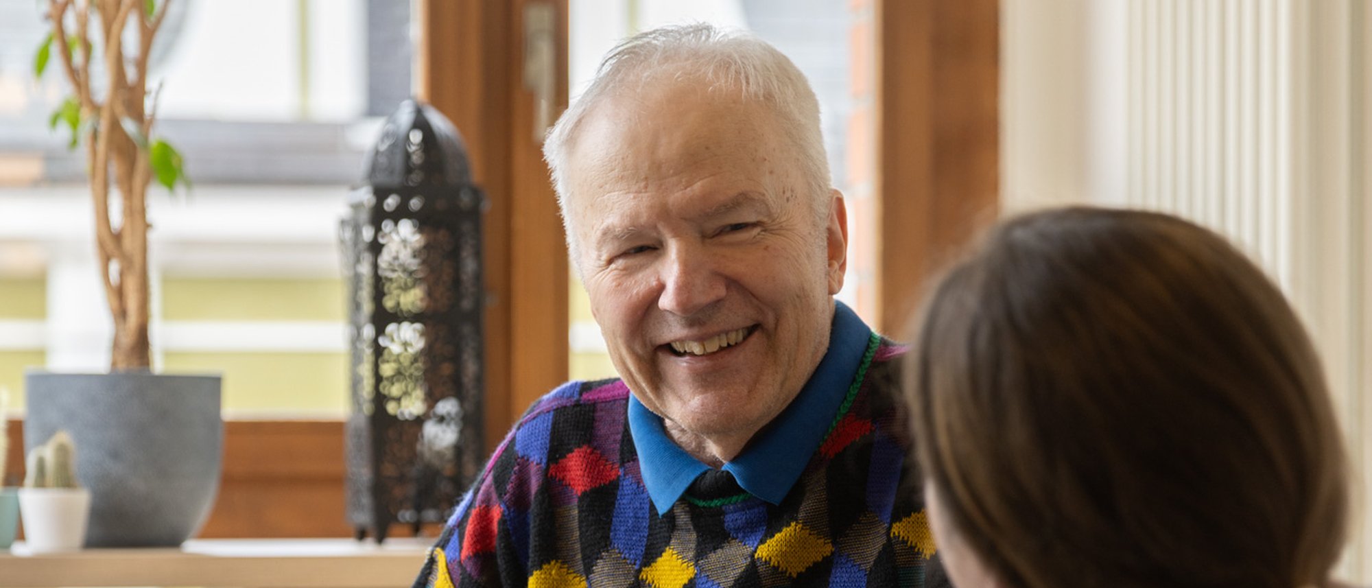 Bewohnender lächelt eine Pflegekraft an, welche der Kamera mit dem Rücken zugewandt ist.