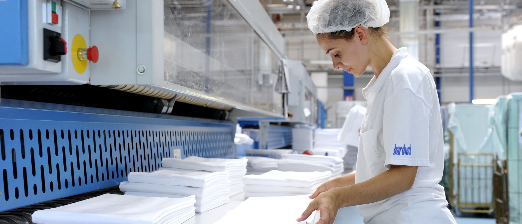 Eine Mitarbeitende in der Wäscherei sortiert und faltet weisse Tücher.
